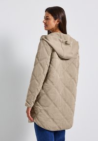 Beige gewatteerde jas met een capuchon, met een diamanten patroon, lange mouwen en verstelbare hardware bij de hals.