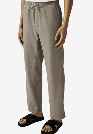 Pantalones beige de cintura elástica con cordón, que presentan un diseño de pierna recta y una tela texturizada, combinados con sandalias negras.