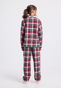 Pijamas de franela a cuadros rojos y verdes, con una parte superior abotonada y pantalones largos. Textura suave con líneas blancas en contraste en el patrón.