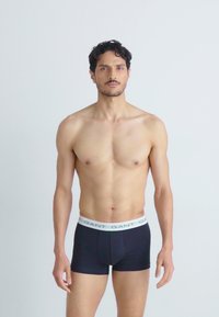 Sorte boxer shorts med en hvit elastisk midje som har merkevarenavnet gjentatt i grønt. Glatt tekstur og tettsittende form.