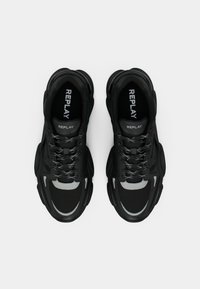 Black sneakers made of mesh and synthetic material, featuring a thick sole, contrasting gray accents, and prominent branding on the tongue.