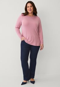 Long-sleeve pink top paired with dark blue jeans. The top has a relaxed fit and smooth texture, with a slight twist detail at the waist.