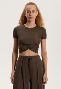 Top scurt, cu mâneci scurte, de culoare maro, cu detaliu strâns în față. Material moale și elastic completează o pereche de pantaloni largi maro, cu un cordon la talie.