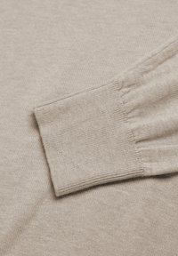 Beige gestrickter Pullover mit gerippten Bündchen, weichem Griff und glatter Oberfläche, der die feine Webart und die Dehnbarkeit des Stoffs zur Geltung bringt.