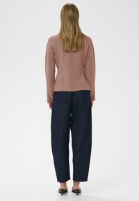 Helles rosa Sweatshirt mit langen Ärmeln, weicher Textur, kombiniert mit dunkelblauen weit geschnittenen Jeans. Schwarze Slipper runden das Outfit ab.