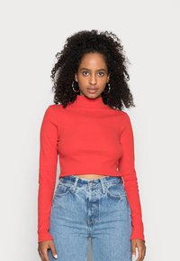 Top cropped canelado vermelho com gola alta e mangas longas, combinado com jeans de cintura alta de cor azul clara com fecho de botão e ligeiro desbotamento.