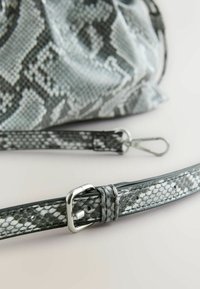 Geantă cu un model de piele de șarpe gri și negru, cu un finisaj texturat. Curea ajustabilă cu o cataramă și clipsuri argintii pentru atașare.