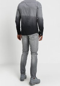 Camisa a cuadros con degradado de gris oscuro a claro, combinada con jeans gris claro y zapatillas grises, vista desde la parte posterior.