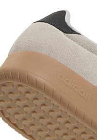 Baskets avec une tige en daim gris clair, un accent noir et une semelle en caoutchouc gomme texturée avec des motifs circulaires. Marque visible sur le côté.