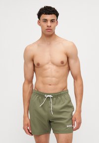 Shorts de bain verts en tissu léger, dotés d'une taille élastique avec cordon de serrage et d'un logo brodé blanc en bas à gauche.