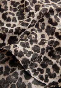 Tkanina w wzór zwierzęcy z kremowym tłem i czarnymi oraz ciemnobrązowymi plamami w leopardzie. Tekstura wydaje się miękka i lekko pomarszczona.