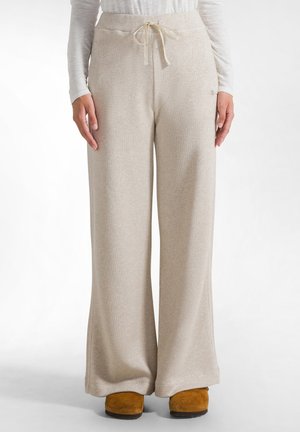 Beigeweite Hosen aus weichem Material mit einem Kordelzugbund, dezentem Glanz und einer lockeren Passform. Die Schuhe sind beige Slipper.