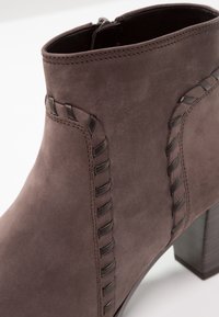 Bottine en daim marron avec bordure tissée sombre décorative et talon bloc sur fond blanc.