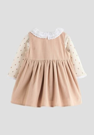 Bruine corduroy jurk met elastische taille, lange mouwen met een witte bloemenprint en een gerimpelde witte kraag. Achterkant detail zichtbaar.