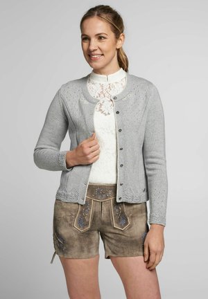 Graue Strickjacke mit rundem Halsausschnitt, detailliertem Muster am Saum und Knopfverschluss, getragen über einem weißen Spitzenoberteil und braunen Shorts.