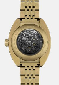 Gouden roestvrijstalen horloge met een gestructureerde, geweven armband en een transparante achterkant die ingewikkelde mechanische bewegingen onthult.