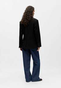 Juodas švarkas su prisiūtu siluetu, su ventiliacija nugaroje, derinamas su plačiomis mėlynomis džinsinėmis kelnėmis ir juodais batais. Lygus, glotnus audinys.