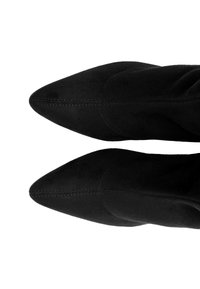 Bottes noires en daim à bout pointu avec des coutures visibles, une texture lisse et un design épuré, mettant en valeur une silhouette ajustée.