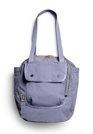 Sac fourre-tout violet clair avec longues anses, poche frontale à rabat sécurisée par deux boutons-pression, et poches latérales sur fond blanc.