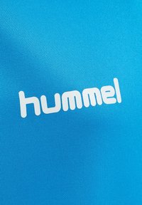 Tessuto blu con una vista ravvicinata del logo bianco del marchio "hummel" stampato su di esso.