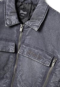 Chaqueta gris oscuro con cremallera y grandes bolsillos delanteros, "Utopia" bordado en la solapa del bolsillo izquierdo y en la etiqueta del cuello, talla pequeña.