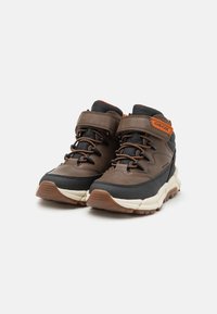 Chaussures de randonnée marron et noires en matériaux textile et cuir. Elles possèdent une sangle velcro, des accents orange et une épaisse semelle en caoutchouc.