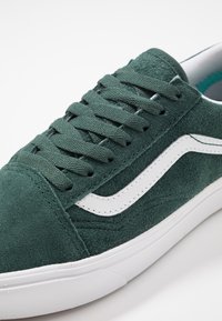 Baskets en daim vert foncé avec une bande blanche sur le côté, des lacets verts assortis et une semelle en caoutchouc blanche sur fond blanc.