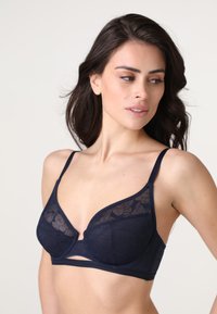 Reggiseno blu navy con coppe in pizzo floreale trasparente e spalline regolabili, caratterizzato da un dettaglio centrale a taglio e una fascia liscia. Texture in tessuto morbido.
