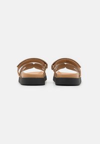Bruna lädersandaler med öppen baksida och utskärningsdesign. Sula i svart, platt och gjord av ett strukturerat material. Justerbar rem.