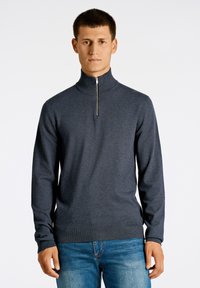 Tummanharmaa neulepaita, jossa on korkea kaulus ja hopeavetoketju. Valmistettu pehmeästä neulekankaasta, jossa on ribattu helma ja hihansuut. Yhdistetty sinisiin farkkuihin.