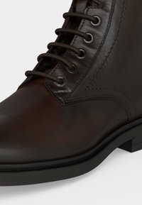 Gros plan d'une botte en cuir marron foncé à lacets avec des œillets métalliques et une semelle noire robuste.