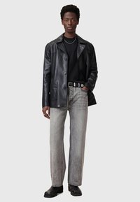Black leather jacket with a button closure, gray denim jeans, and black ankle boots. Model stands against a neutral background.