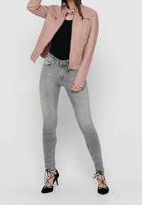 Světle růžová kožená bunda s přiléhavým střihem, kombinovaná se šedými skinny džíny a černými vysokými podpatky. Hladká textura, minimální kovové prvky.