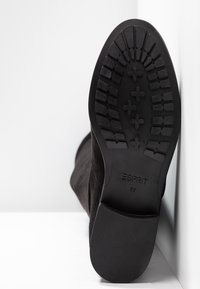 Semelle d’une botte noire Esprit avec grip texturé et taille 37 marquée, inclinée contre une surface blanche.