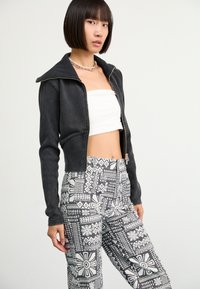 Black cropped jacket with a high collar, paired with high-waisted pants featuring a white geometric pattern on a black background.