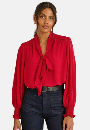 Rote Bluse mit Schleifenkragen, langen Puffärmeln und Rüschendetails. Glatter Stoff mit subtilen Raffungen an der Schulter und den Manschetten.