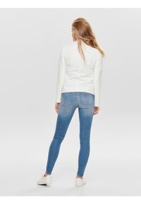 Bíle přiléhavé sako spárované s modrými džíny skinny. Džíny mají vybledlou texturu a jsou doplněny bílými teniskami.