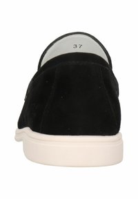 Scarpe slip-on in suede nero con suola in gomma bianca. L'interno presenta un'etichetta con la taglia 37. Il design è minimalista, senza pattern visibili.