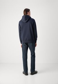 Navy blue hooded sweatshirt with a textured fabric, paired with dark denim jeans and black shoes, viewed from the back.