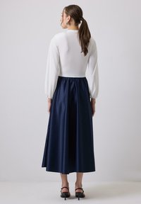 Abito lungo con un corpetto bianco aderente e una gonna in satin blu navy voluminosa. Le maniche sono a sbuffo e raccolte ai polsi.