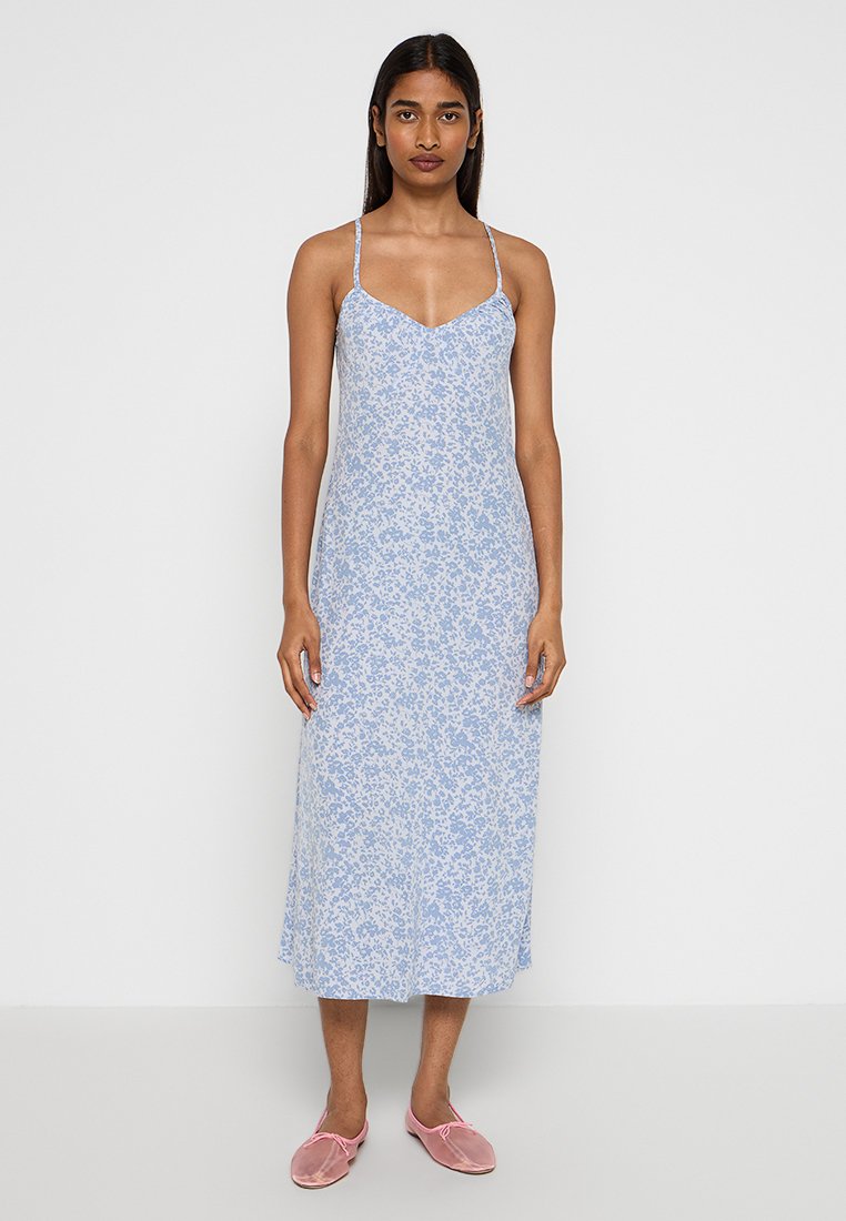 Hellblaues Blumen-Kleid mit dünnen Trägern, knielang, aus weichem Stoff und in lockerem Schnitt. Kombiniert mit pinken Slippern.