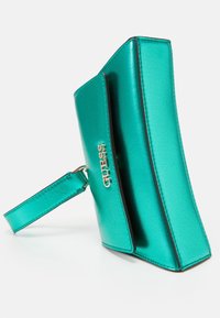 Teal metallic clutch bag with a sleek design, featuring a shoulder strap and embossed "GUESS" logo in gold. Smooth texture and angular shape.
