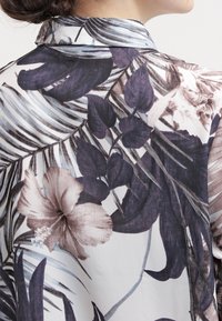 Floral-patterned blouse with dark purple and beige hibiscus flowers, large leaves, and a soft, lightweight fabric. Features a classic collar.