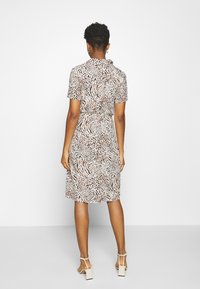 Donna in piedi di spalle che indossa un vestito a stampa animale lungo fino al ginocchio e sandali con tacco beige su uno sfondo semplice.