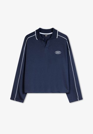 Tamsiai mėlynas ilgomis rankovėmis polo marškinėliai, su apykakle, balta apdaila aplink kraštus ir logotipu ant krūtinės. Pagaminta iš medvilnės mišinio.