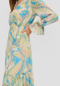 Langes, farbenfrohes Kleid mit einem Paisleymuster in Blau-, Gelb- und Pinktönen. Aus leichtem Stoff gefertigt, mit weit ausgestellten Ärmeln und einem taillierten Bund.