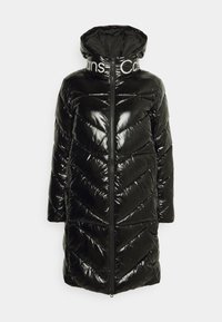 Svart puffjacka med en glänsande yta, mönster i chevron-kviltning, hög krage och dragkedja. Varumärkeslogotypen syns på kragen.