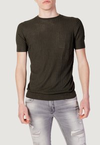Maglietta a maniche corte di colore verde scuro, a coste, con collo rotondo e taschino sul petto. Indossata con jeans grigi chiari strappati.