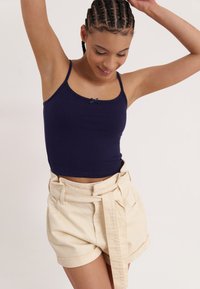 Marineblå ribbet tanktop med en scallop-halslinje og lille sløjfedetalje, parret med højtaljede, beige shorts med bælte.