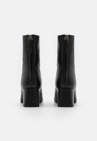 Černé kožené kotníkové boty se čtvercovým podpatkem, s centrálním zipem na zadní straně a hladkým, matným povrchem.